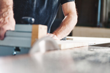 Carpenter using woodworking machinery cutting plank of wood