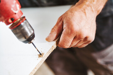 Carpenter using drill driver while working on white wooden plank