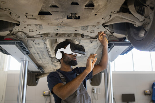 Mechanic wearing virtual reality headset performs 3D inspection of car to find malfunction in modern garage setting. Innovative technology aiding automotive repair work.