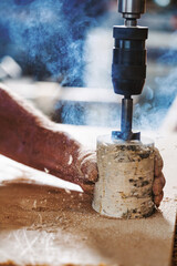 Carpenter drilling hole in wood with power drill in workshop