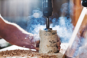 Carpenter drilling hole in wood with power drill creating sawdus