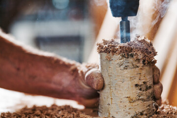 Carpenter drilling hole in birchwood using drill press in worksh