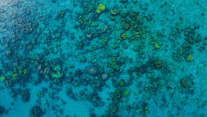 Top view. Summer sea water, blue surface. The water is clear with ripples and sparkles in the sunlight and you can see coral under the sea	