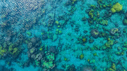 Top view. Summer sea water, blue surface. The water is clear with ripples and sparkles in the sunlight and you can see coral under the sea	