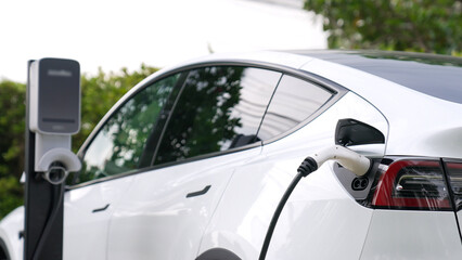 EV electric car recharge battery at parking lot in natural green city park. Alternative clean energy technology for rechargeable automobile for sustainable and eco friendly urban travel. Synchronos