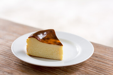 Close up a piece of Basque burnt cheesecake on white dish and wooden table.