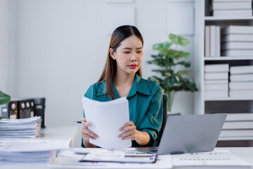 Asian woman in the workplace Work Hard writing notes on a pad from her laptop computer with analytical charts and graphs in front of her, business people concept