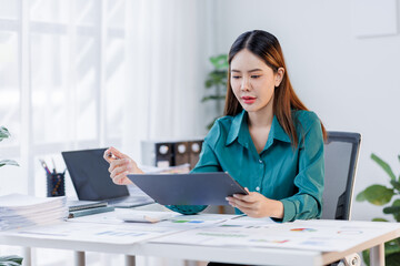 Asian woman in the workplace Work Hard writing notes on a pad from her laptop computer with analytical charts and graphs in front of her, business people concept