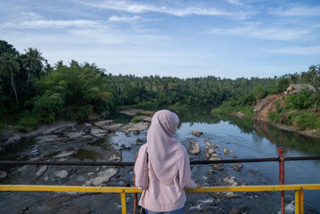 A woman stands on a suspension bridge over a river