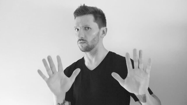 Footage of a man lifting up his arms in a manner that says stop it, do not do it and to hold on in slow motion shot in 4K resolution. Footage is black and white and the man has short hair and a beard.