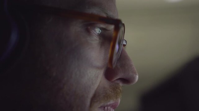 man wearing glasses focused on screen of computer or smartphone. concentrating at work reading or watching a video. Side shot of guy staring at a bright light screen. close up 