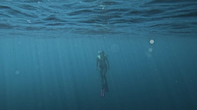 female freediver going up in epic wide oceanic shot, sunny light rays through water surface