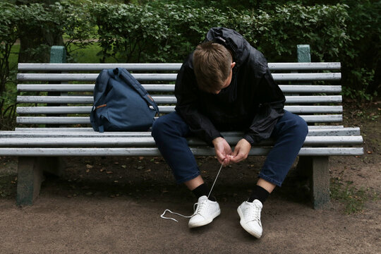 A teenage boy on a bench tying his shoelaces. - Powered by Adobe