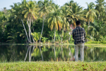 Obraz premium A man is fishing alone near a swamp with a coconut plantation in the background