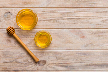 Glass jar of honey with wooden drizzler on colored background. Honey pot and dipper high above. Top view copy space