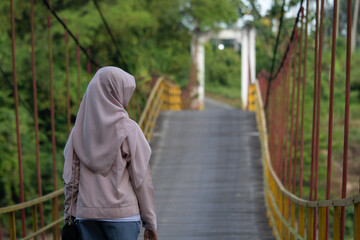A woman walks along a suspension bridge over a river