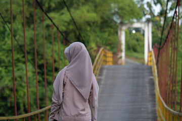 A woman walks along a suspension bridge over a river