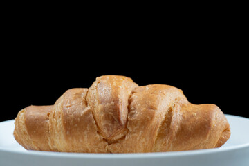 close shot of croissant in white plate isolated black background