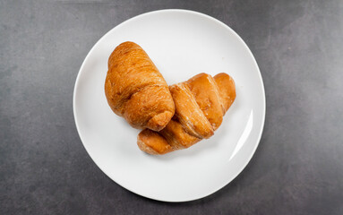top view of pile of croissants in white plate on dark stone table