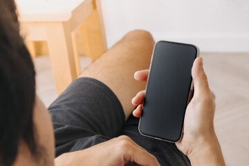 Top view of asian man using and holding mobile phone, showing empty black screen while sitting in room apartment.