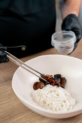 fast food establishment large chef in a black uniform prepares Japanese udon soup from previously...