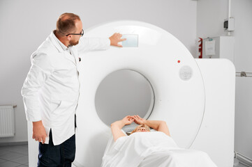 Medical computed tomography or MRI scanner. Male radiologist pointing MRI screen to examine female...