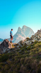 Obraz premium Impressive view from the ascent to Espelunciecha Peak in the Pyrenees, with a young man enjoying the Ibón de Anayet, Anayet Peak and the imposing Midi d'Ossau in the background. 