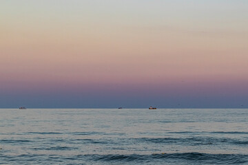 calm sea at dawn, bright colors of the sky, boats in the distance on the horizon