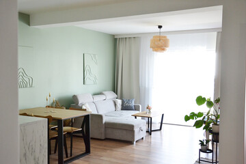 Przytulny salon jadalnia z miętową zieloną ścianą obrazami i wygodną szarą sofą i zasłonami i firaną i sztuką line art © VILKTERIO