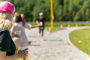 Obraz premium A volunteer girl in a dark shirt holds out a plastic cup of water to a triathlon runner.