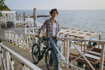 Fototapeta premium Full body side profile view minded young woman she wears shirt casual clothes walk stroll with bicycle rest near sea ocean sand shore beach outdoor seaside in summer day free time. Lifestyle concept.