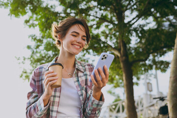 Young woman wear shirt casual clothes hold use mobile cell phone drinking coffee sits walk rest...