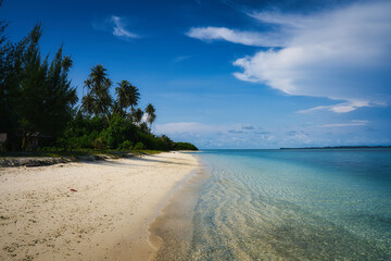 Untouched beautiful beach of Sikandang Island in Sumatra, where pristine sandy beaches meet crystal clear waters, framed by lush palm trees under a vibrant blue sky.