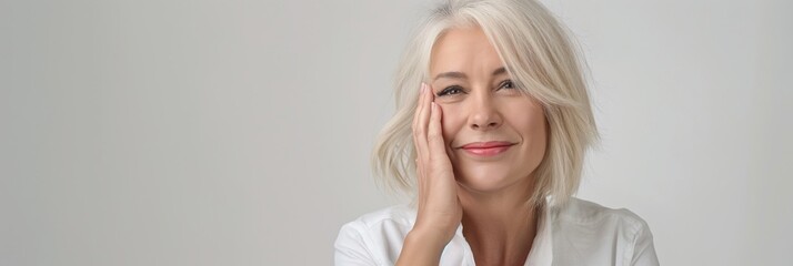 An elderly woman with graceful gray hair exudes joy and confidence, smiling peacefully in a white shirt. Her pose radiates contentment and elegance, portraying a positive lifestyle