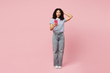 Full body happy surprised shocked fun little kid teen girl wears blue striped t-shirt casual clothes hold head use mobile cell phone isolated on plain pastel light pink background. Childhood concept.