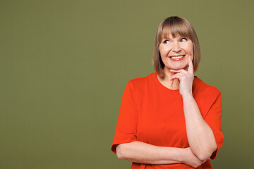 Elderly blonde woman 50s years old she wear orange t-shirt casual clothes put hand prop up on chin, lost in thought and conjectures isolated on plain pastel green background studio. Lifestyle concept.