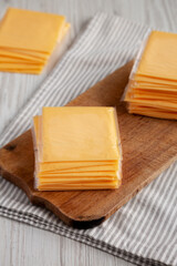 Yellow Cheddar American Cheese Stacked Slices on a wooden board, side view.