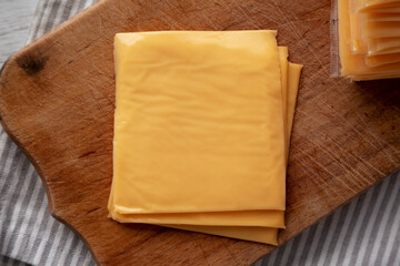 Yellow Cheddar American Cheese Stacked Slices on a wooden board, top view.