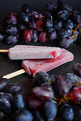 Two berry-grape popsicles next to clusters of dark grapes on a dark background