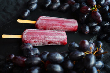 Two berry-grape popsicles next to clusters of dark grapes on a dark background