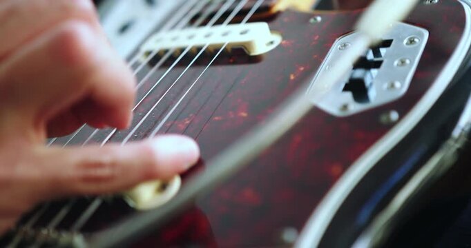 Beautiful slow motion detail shot of hands rhythmically plucking the strings of an electric guitar in a recording studio with natural light coming in from the balcony.