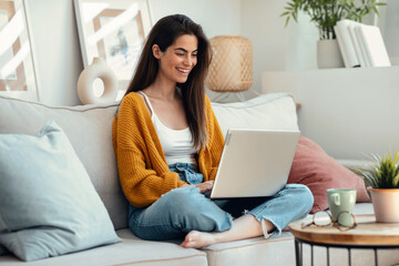 Beautiful young woman working with her laptop while sitting on a couch at home.