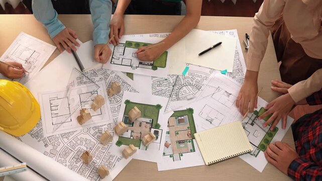 Architect and safety engineer discussion about building construction use blueprint on table with architectural document, measurement tool and wooden block scatter around at modern office. Delineation.