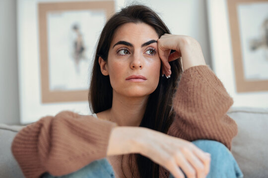 Depressed young woman overthinking while sitting on the couch at home