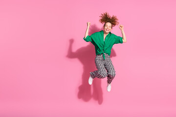 Photo of lucky attractive lady dressed green shirt jumping high rising fists empty space isolated pink color background