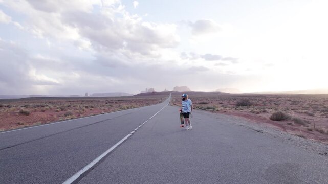 Man And His Longboard Walking On Forrest Gump Point Road Towards Monument Valley In Utah, United States. pull-back shot