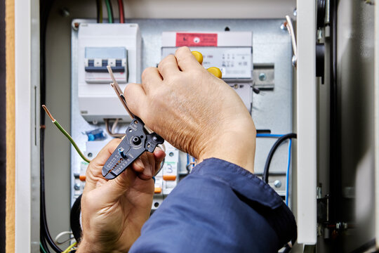 Electrical installation work on connecting power cable to an outdoor electrical cabinet, installer cleans ends of wires from insulation using stripper cutter tool.