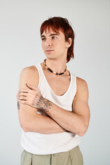 Trendy young man with vibrant red hair strikes a pose in a white tank top against a grey studio backdrop.