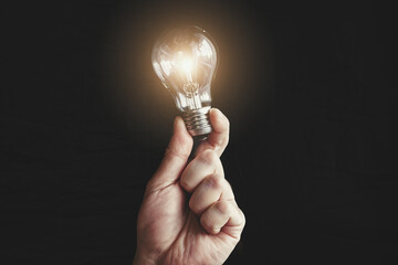 A man's hand holding a light bulb in the dark for innovation and creative concept. Power outage in...
