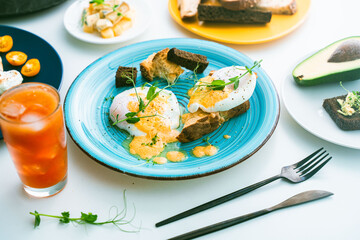 Eggs, Benedict on bread toast and avocado on a slice of rye bread, cheese and a glass of orange juice on the table. Selected focus.